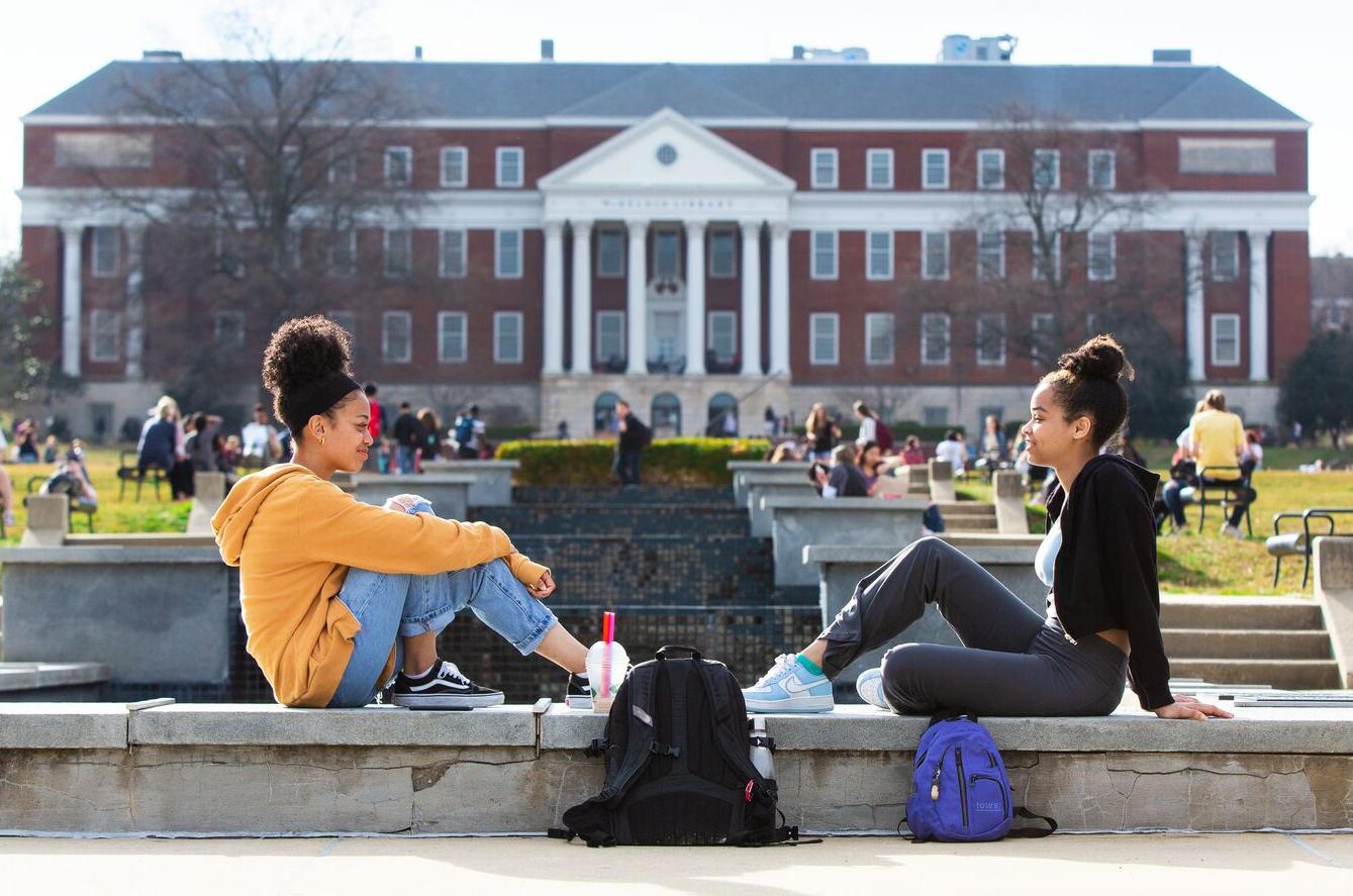 Two students sit facing each other on the ODK Fountain on McKeldin Mall